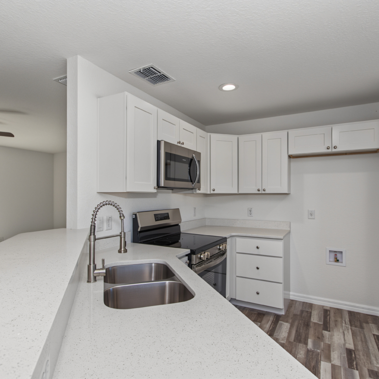 Close-up of undermount stainless steel double sink and high-arc faucet on white granite countertop.