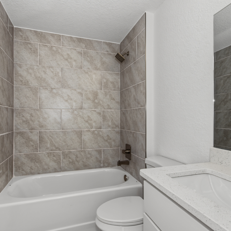 Guest bathroom featuring tub with grey tile surround, toilet, and single vanity mirror