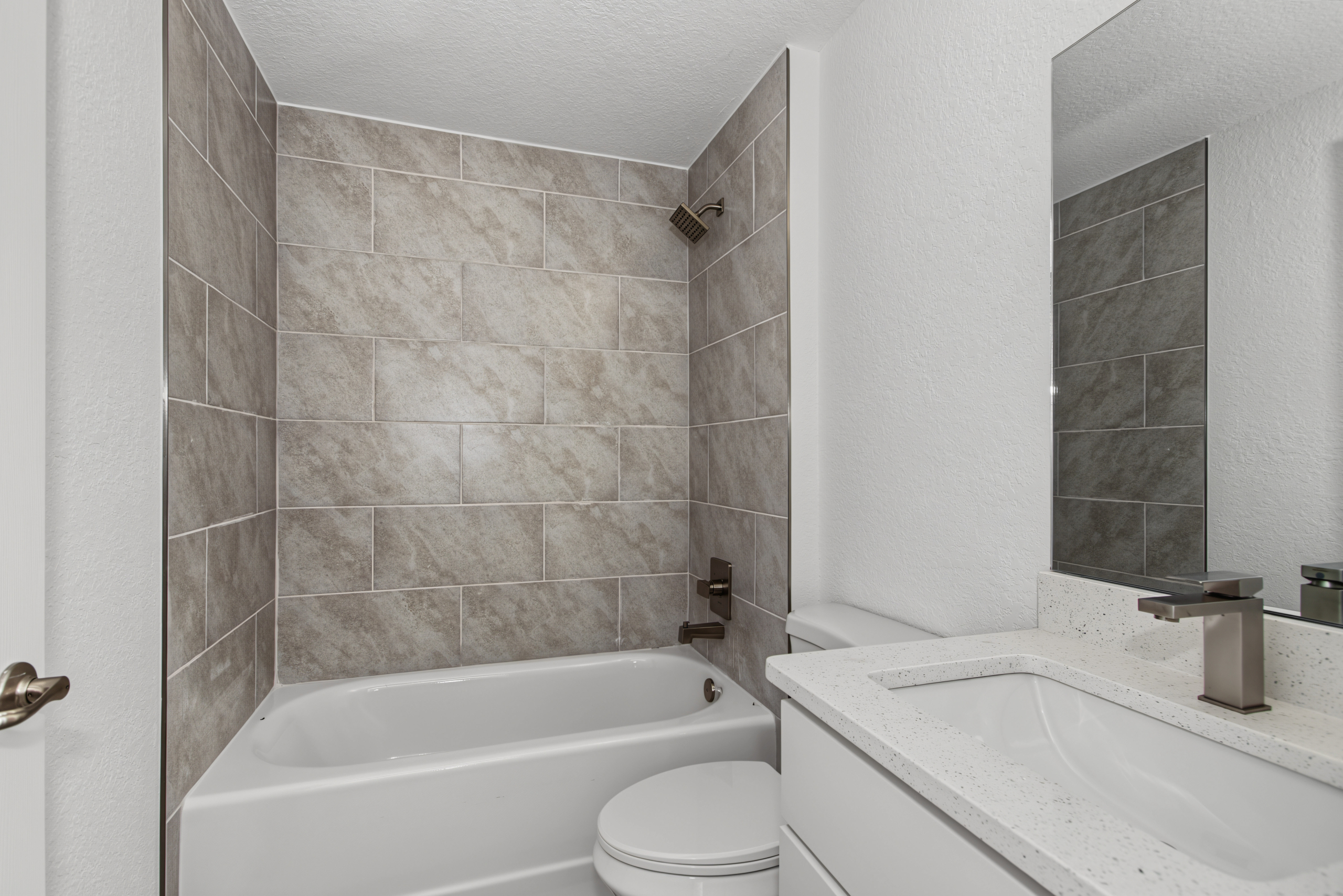 Guest bathroom featuring tub with grey tile surround, toilet, and single vanity mirror