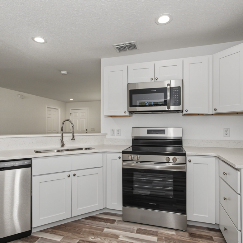 Kitchen design with white cabinetry, granite counter space, built-in microwave, and stainless steel stove.