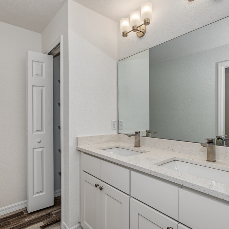 Primary bathroom featuring double sink vanity with granite countertops, wide mirror, and view into bedroom.