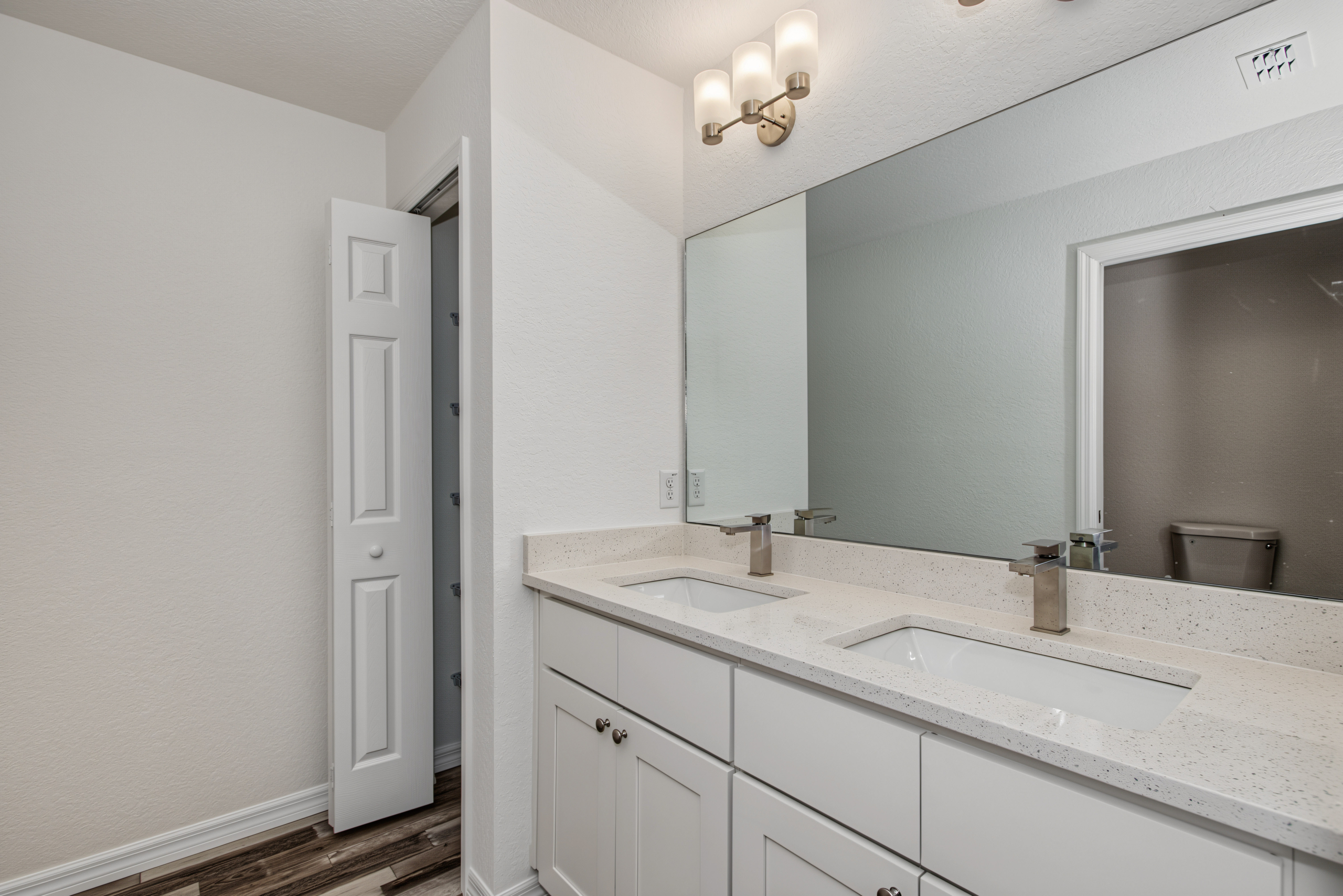 Primary bathroom featuring double sink vanity with granite countertops, wide mirror, and view into bedroom.