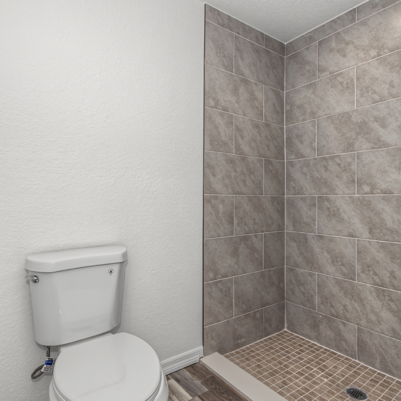 Primary bathroom walk-in shower with tiled walls and mosaic floor next to white toilet.